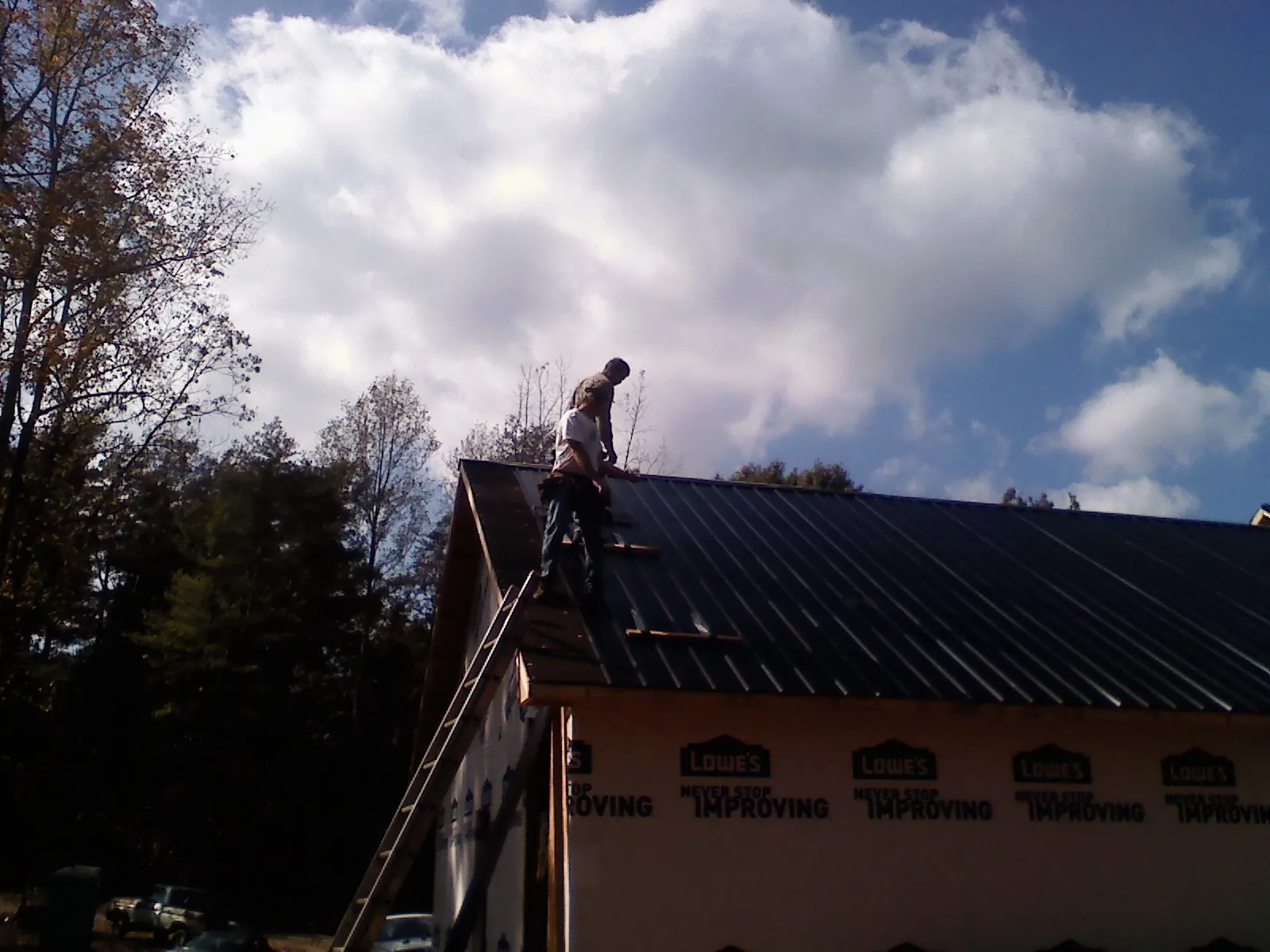 Roofer fastening dark metal panels high against a cloudy sky, from a Roof Inspection job in Lincoln City