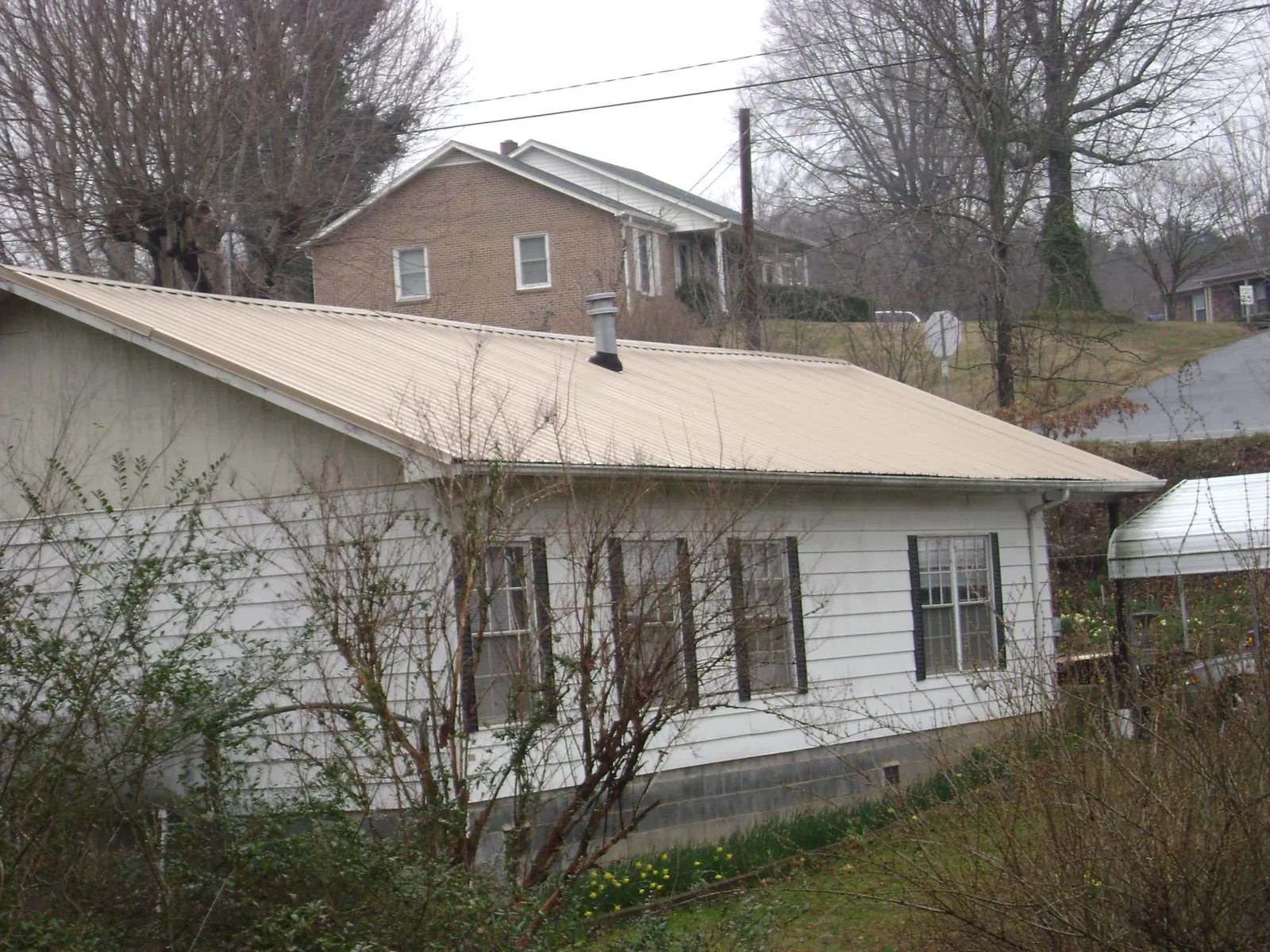 Tan metal roof on a white sided house set into a hillside — Commercial Roofing by Roofing Brothers in Lincoln City